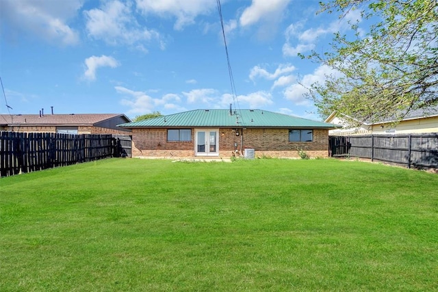 rear view of property with brick siding, a fenced backyard, a lawn, and metal roof