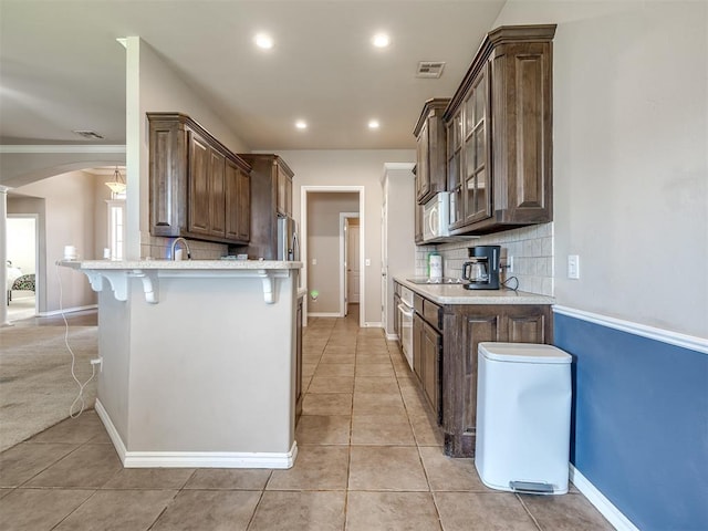 kitchen featuring a kitchen breakfast bar, arched walkways, light tile patterned floors, white microwave, and a peninsula