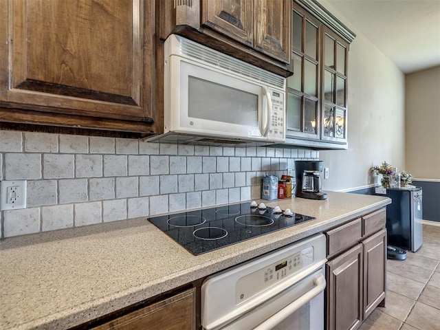 kitchen with light countertops, dark brown cabinets, white appliances, and tasteful backsplash