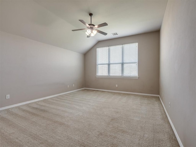 empty room featuring ceiling fan, light colored carpet, visible vents, baseboards, and lofted ceiling