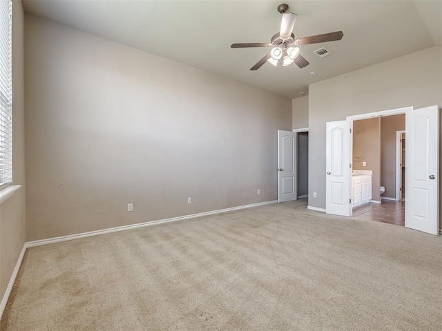 unfurnished bedroom featuring visible vents, baseboards, ensuite bathroom, a high ceiling, and light colored carpet