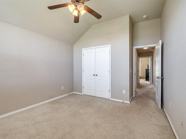 unfurnished bedroom with light colored carpet, a ceiling fan, baseboards, vaulted ceiling, and a closet