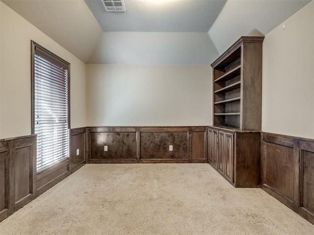 unfurnished office with carpet flooring, visible vents, wainscoting, and lofted ceiling