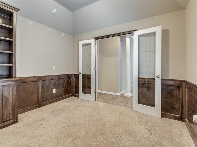 unfurnished bedroom with wainscoting, carpet, french doors, and lofted ceiling