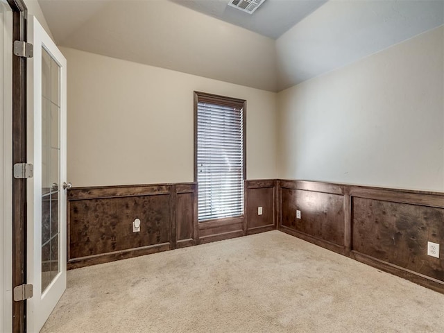 unfurnished room with a wainscoted wall, carpet flooring, lofted ceiling, and visible vents