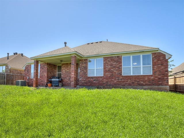 rear view of property with fence, a shingled roof, brick siding, cooling unit, and a lawn