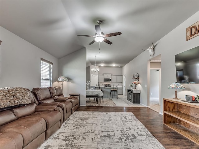 living room with lofted ceiling, wood finished floors, baseboards, and ceiling fan with notable chandelier