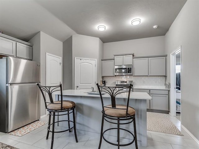 kitchen with a kitchen bar, stainless steel appliances, decorative backsplash, and gray cabinets
