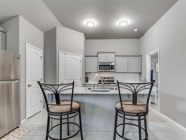 kitchen with a kitchen breakfast bar, a sink, appliances with stainless steel finishes, gray cabinetry, and backsplash