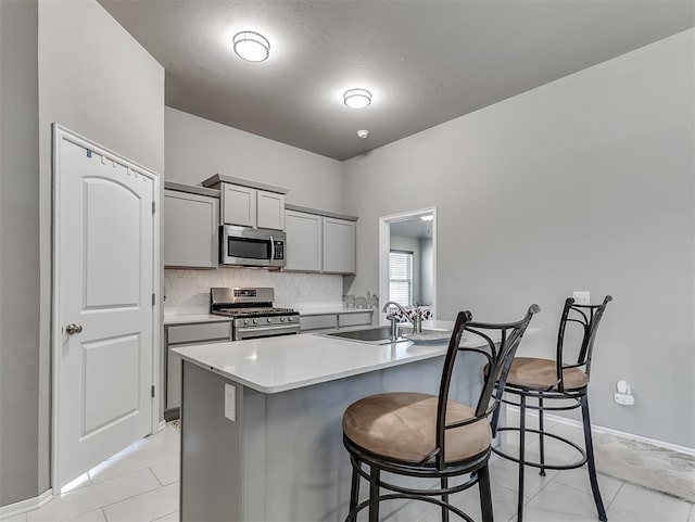 kitchen with a sink, a kitchen bar, light countertops, gray cabinetry, and appliances with stainless steel finishes
