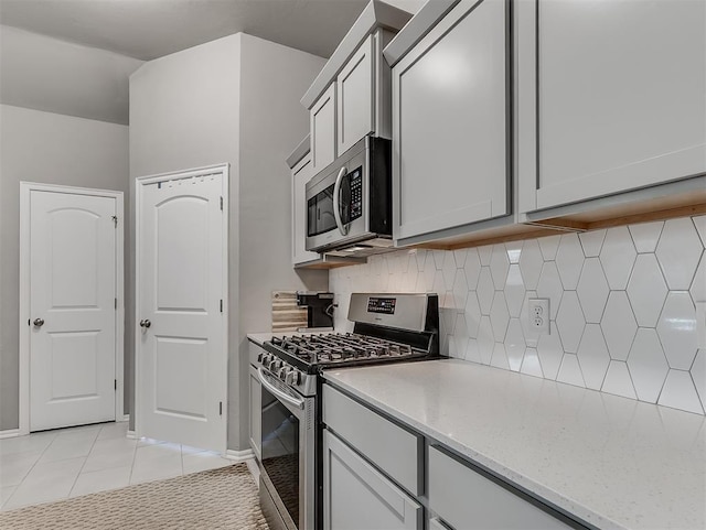 kitchen with light stone counters, light tile patterned floors, decorative backsplash, stainless steel appliances, and baseboards