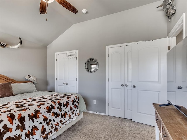 bedroom with ceiling fan, multiple closets, vaulted ceiling, and light colored carpet