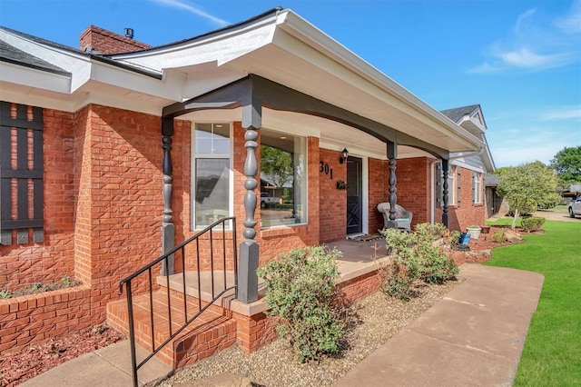 entrance to property with brick siding, a porch, and a chimney