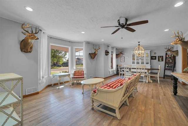 living room featuring visible vents, light wood-style flooring, recessed lighting, and ceiling fan with notable chandelier