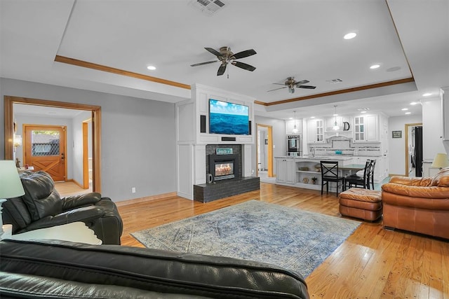 living room with light wood-type flooring, visible vents, ceiling fan, and a raised ceiling