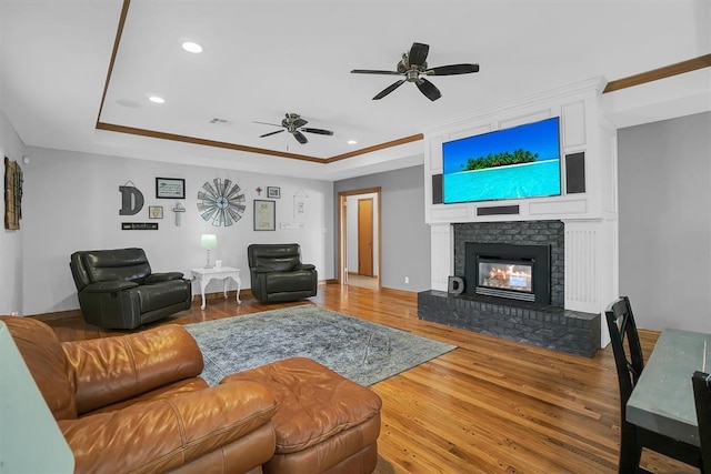 living room with ceiling fan, a fireplace, a tray ceiling, recessed lighting, and wood finished floors