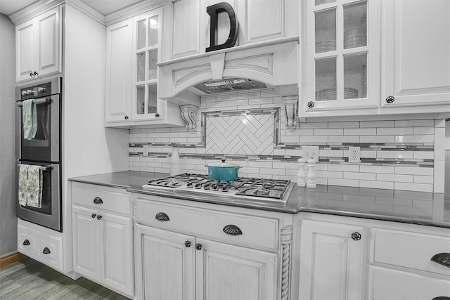 kitchen with backsplash, white cabinets, appliances with stainless steel finishes, and premium range hood