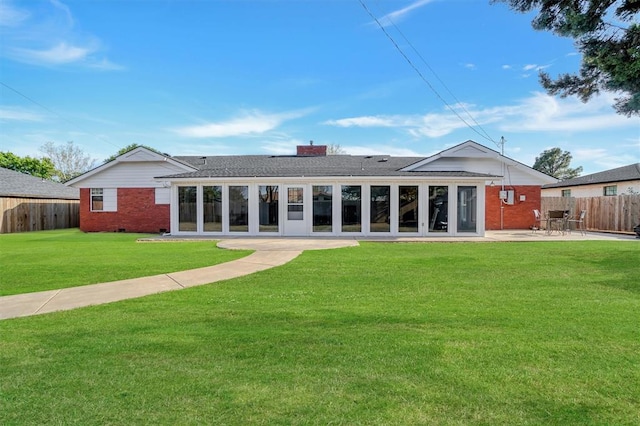 rear view of house with a patio, a chimney, brick siding, fence, and a lawn