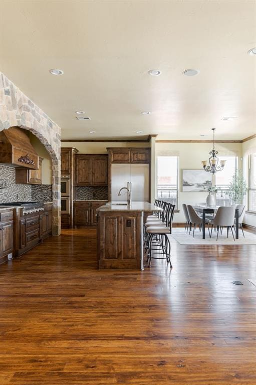 kitchen featuring decorative backsplash, a kitchen island with sink, appliances with stainless steel finishes, and dark wood-style flooring
