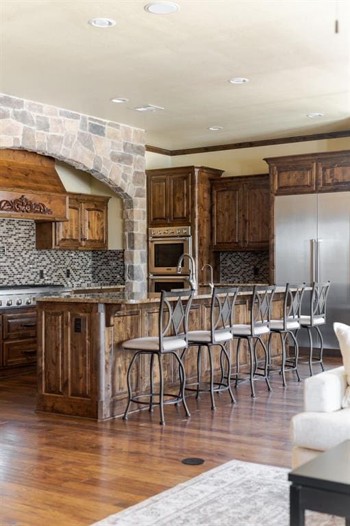 kitchen featuring dark wood-type flooring, backsplash, a breakfast bar area, and stainless steel appliances