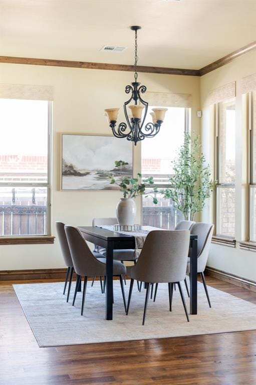 dining room with crown molding, wood finished floors, a notable chandelier, and visible vents