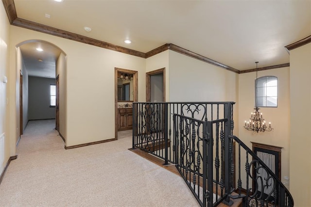 hallway with baseboards, arched walkways, ornamental molding, an upstairs landing, and light colored carpet