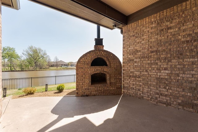 view of patio / terrace with a water view, fence, and an outdoor brick fireplace