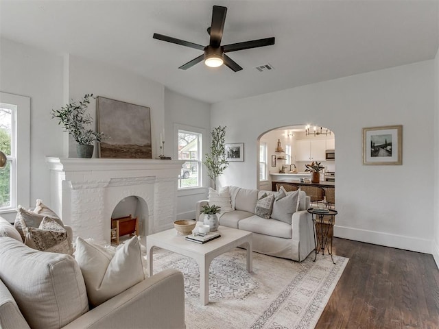 2431 NW 13th St, Oklahoma City, OK 73107 - living area with arched walkways, dark wood-style flooring, a ceiling fan, and a brick fireplace
