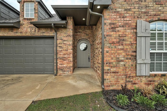 view of exterior entry with roof with shingles, driveway, and brick siding