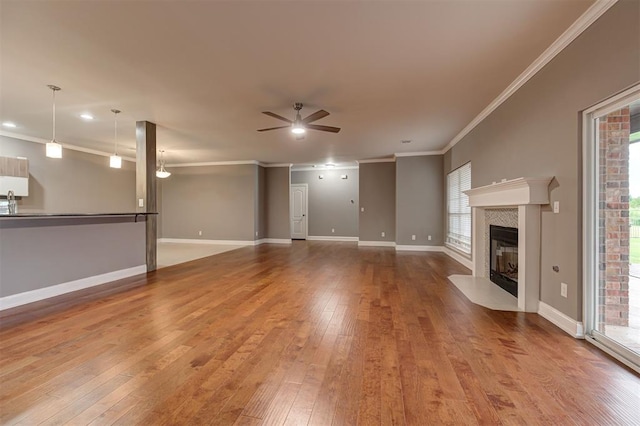 unfurnished living room featuring crown molding, wood-type flooring, ceiling fan, a wealth of natural light, and a premium fireplace