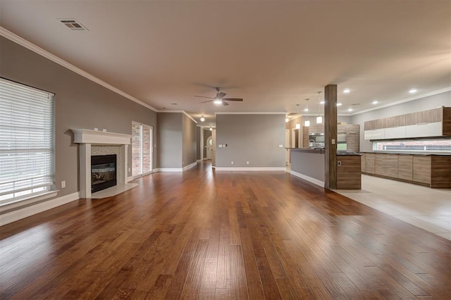 unfurnished living room with ceiling fan, visible vents, crown molding, a fireplace, and hardwood / wood-style floors