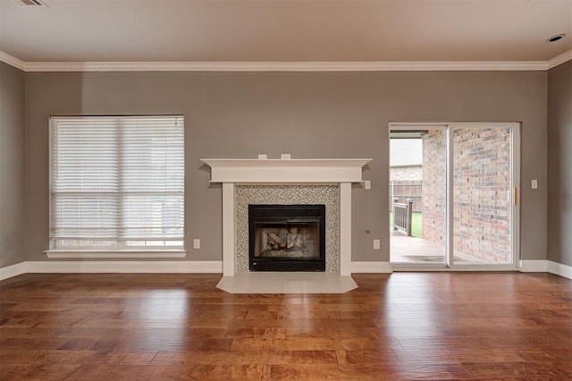 unfurnished living room with baseboards, wood finished floors, a tile fireplace, visible vents, and ornamental molding