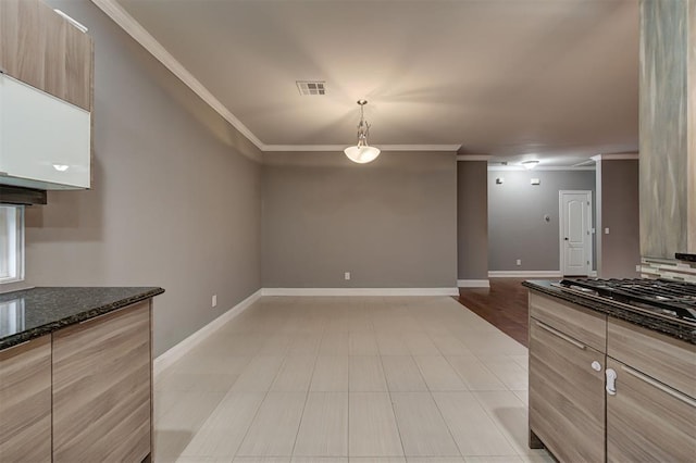 kitchen with baseboards, ornamental molding, dark stone countertops, and stainless steel gas cooktop