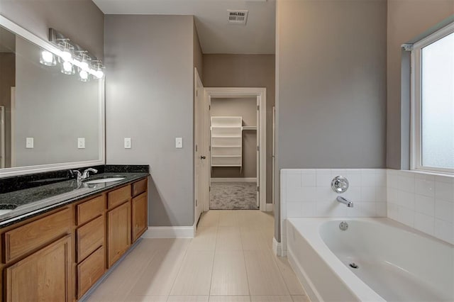 bathroom with double vanity, a garden tub, visible vents, baseboards, and a spacious closet