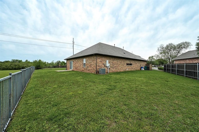 exterior space featuring brick siding, a fenced backyard, central AC, and a yard