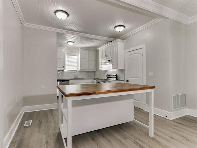kitchen with butcher block countertops, appliances with stainless steel finishes, ornamental molding, and visible vents