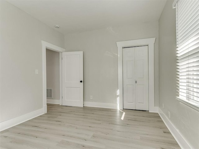 unfurnished bedroom with a closet, visible vents, light wood-type flooring, and baseboards