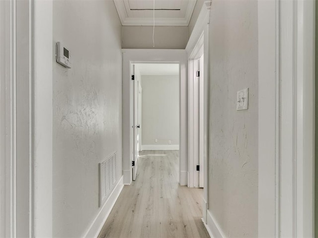 corridor with baseboards, light wood-type flooring, ornamental molding, attic access, and visible vents
