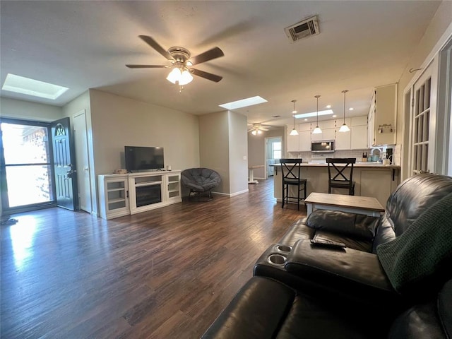 136 Skyline Dr, Chickasha, OK 73018 - living area with visible vents, baseboards, dark wood-style flooring, a ceiling fan, and a skylight