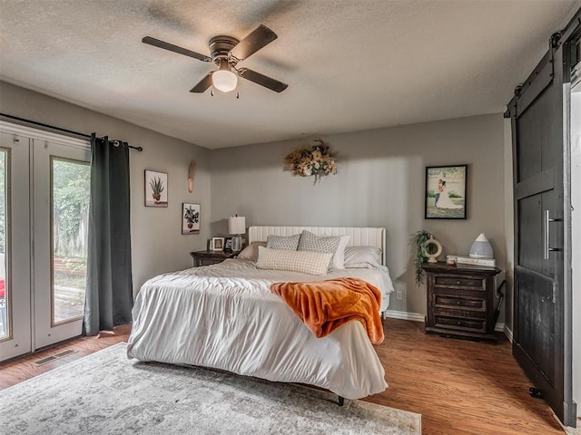 7 Kaross Dr, Shawnee, OK 74801 - bedroom featuring a barn door, wood finished floors, access to outside, a textured ceiling, and ceiling fan