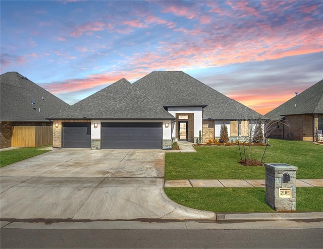 view of front of property with a garage, roof with shingles, driveway, and a lawn