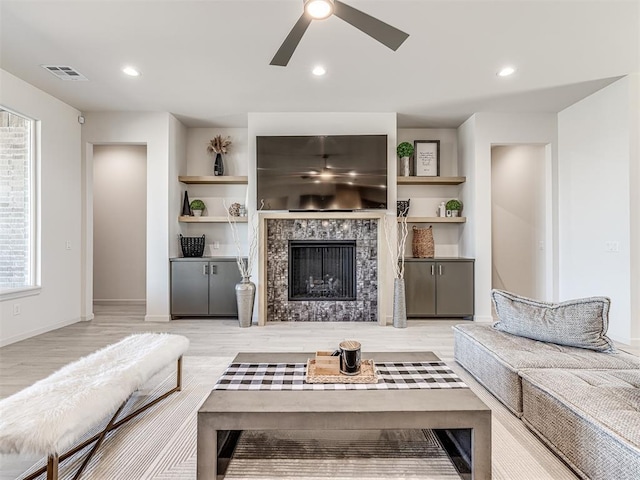 living area with light wood-style flooring, a ceiling fan, visible vents, a tiled fireplace, and baseboards