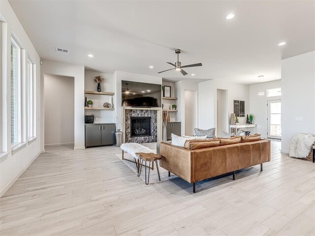 living area with visible vents, baseboards, a ceiling fan, light wood-style floors, and a fireplace