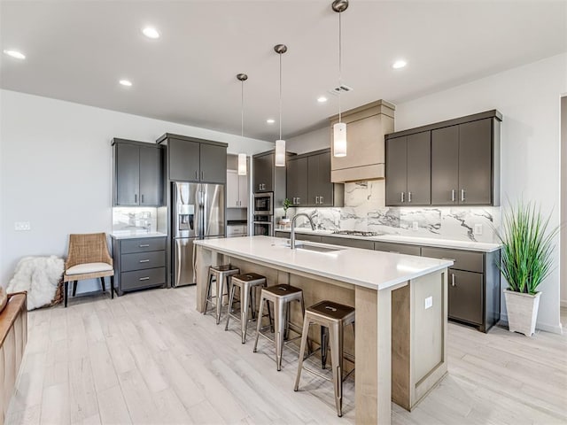 kitchen with appliances with stainless steel finishes, a sink, light wood finished floors, a breakfast bar area, and backsplash