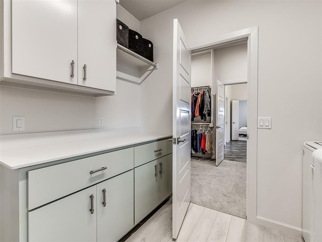 kitchen featuring light wood-type flooring, washer and clothes dryer, light countertops, and white cabinetry