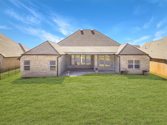 back of house with roof with shingles, brick siding, a fenced backyard, and a lawn