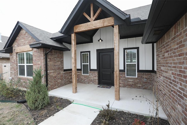 view of exterior entry featuring roof with shingles, brick siding, and board and batten siding