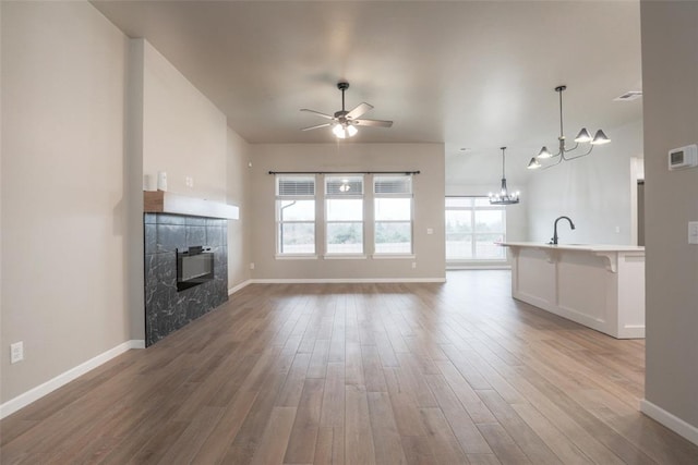 unfurnished living room with a high end fireplace, ceiling fan with notable chandelier, baseboards, and wood finished floors