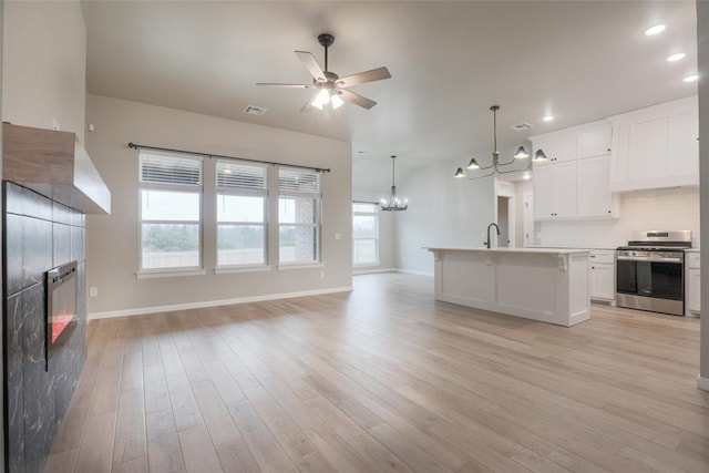 kitchen featuring a tiled fireplace, open floor plan, light countertops, stainless steel range, and ceiling fan with notable chandelier