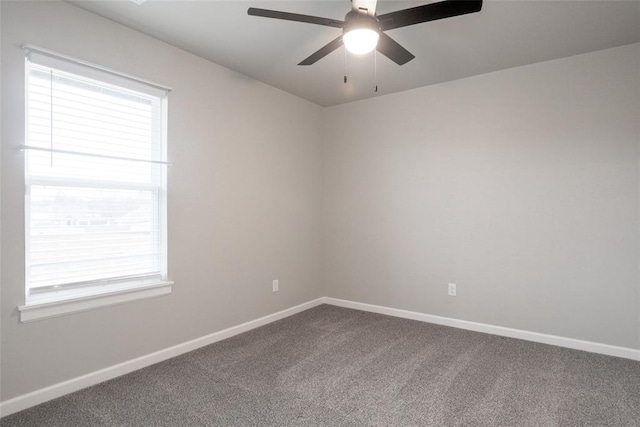 spare room featuring dark colored carpet, ceiling fan, baseboards, and a healthy amount of sunlight